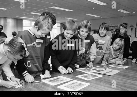 Judging newspaper photos IJC editorial team [IJmuider Courant], Whizgle News, Dutch Desk, The Netherlands, 1950 - 2000 on 27-11-1992. The image includes these topics. In a well-lit classroom, a group of children is engaged in a creative activity around a wooden table. The setting features large windows that allow natural light to fill the room, creating a bright and inviting atmosphere. The walls are adorned with educational materials and art, hinting at a vibrant learning environment. The children, of varying ages, are focused on their task. They display a range of expressions—from concentrat Stock Photo