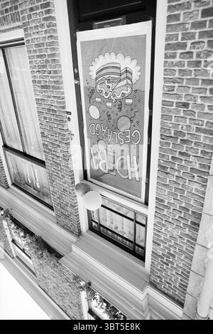 Hooray passed exam, Whizgle News, Dutch Desk, The Netherlands, 1950 - 2000 on 14-06-1995. These are the topics in the image. The scene features a vibrant façade of a building, characterized by its textured brick surface, which creates a rugged yet inviting atmosphere. The brickwork is presented in various shades of brown, creating depth and interest. Dominating the view is a large decorative banner, vividly colored, featuring whimsical graphics that include playful shapes and patterns, hinting at a lively theme. Bright hues such as red, blue, yellow, and green make the banner stand out against Stock Photo