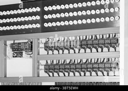 Interior and exterior Switch cabinet Fa. Geert's engineering office, Whizgle News, Dutch Desk, The Netherlands, 1950 - 2000 on 24-12-1968. These are the elements in the image. The scene presents a complex arrangement of electrical components and wiring. At the top section, a series of circular buttons or dials are aligned in neat, uniform rows, suggesting a systematic layout. These circular elements possess a metallic sheen, reflecting light subtly, and are surrounded by a polished surface that enhances their prominence. Below, intricately arranged wiring is visible, with multiple strands conn Stock Photo