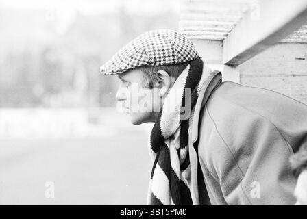 Portrait Barry Hughes trainer FC Haarlem, Whizgle News, Dutch Desk, The Netherlands, 1950 - 2000 on 01-1978. These topics are shown in the image. In the scene, a man leans slightly forward, resting his arm on a surface adorned with a weathered wooden railing. He wears a distinctive cap patterned with black and white checks, which adds a classic touch to his appearance. His complexion is fair, and the subtle lines of his profile hint at a thoughtful demeanor. Draped around his neck is a scarf featuring alternating bold stripes in shades of black and white, providing a striking contrast to his s Stock Photo