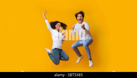Overjoyed multiracial couple jumping in the air and celebrating success Stock Photo