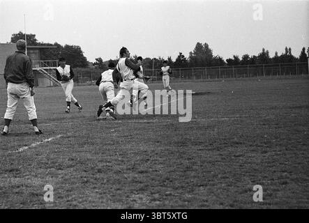 Baseball match RCH- Bloemendaal with Johan Neeskens in a dark sweater. When he still played baseball at RCH. Baseball Heemstede Sportparklaan The Netherlands, Whizgle News, Dutch Desk, The Netherlands, 1950 - 2000 on 26-07-1969. These topics appear in the image. The scene captures a dynamic moment on a grassy athletic field, where the energy of a baseball practice is palpable. Several players in white uniforms with black accents are engaged in various activities. One individual is running towards a base, showcasing movement and urgency, while another appears to be preparing to catch the ball, Stock Photo