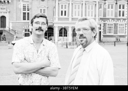 2 organizers Baars and Schoonbeek Haarlem Jazz Jazz Organization. Agency for room rental Haarlem The Netherlands, Whizgle News, Dutch Desk, The Netherlands, 1950 - 2000 on 09-08-1988. The image contains these topics. The scene features two men standing together in a city square, exuding a relaxed yet confident demeanor. One man has a well-groomed mustache and sports a short-sleeve, patterned shirt with a map-like design, while the other wears a neat, long-sleeve dress shirt paired with a tie. In the background, the architecture showcases a blend of classical and modern elements, with large win Stock Photo