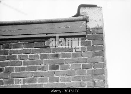 Buildings at Fillipo cracks Haarlem buildings, Whizgle News, Dutch Desk, The Netherlands, 1950 - 2000 on 03-04-1978. These topics are shown in the image. The scene captures a close-up view of a brick wall, where the texture and details of the masonry are prominently featured. The bricks are arranged in a classic pattern, showcasing variations in color ranging from deep red to faded brown, with some bricks appearing weathered and worn. At the top of the wall, there is a wooden ledge, painted a muted gray, which contrasts with the earthy tones of the bricks. This ledge has a slight curve at the Stock Photo