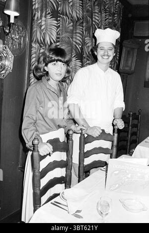 Cook Tamirez with wife Zandvoort Persons Zandvoort, Whizgle News, Dutch Desk, The Netherlands, 1950 - 2000 on 07-08-1979. These topics appear in the image. The scene captures two individuals standing side by side in a cozy, warmly lit indoor setting, likely a restaurant. The background features wooden paneling and tropical-themed wallpaper adorned with palm leaves, which adds a touch of warmth and charm to the atmosphere. One person, a woman with a smooth bob hairstyle, wears a blouse with a modest collar and a distinct striped skirt that matches the classic decor. Her expression is friendly a Stock Photo
