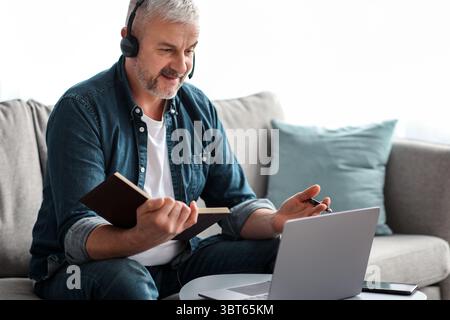Happy old man having online class, using laptop and headset Stock Photo