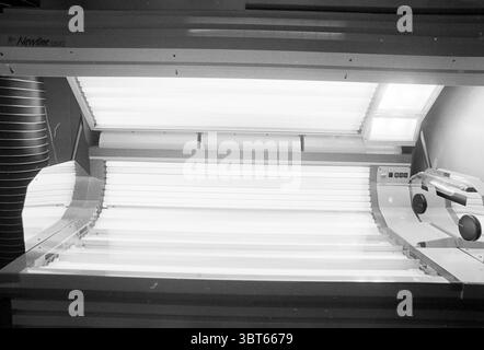 City Sun Centre, Whizgle News, Dutch Desk, The Netherlands, 1950 - 2000 on 14-06-1994. These topics are shown in the image. The scene depicts an indoor tanning bed, characterized by sleek, modern design elements. The device is predominantly white, emphasizing a clean and clinical aesthetic. The tanning bed is elongated, featuring several rows of fluorescent lights that radiate a bright, soft glow. The panels of the tanning bed are smooth and appear to be reflective, enhancing the luminous atmosphere. The lighting is stark, creating sharp contrasts and casting subtle shadows on the surfaces nea Stock Photo