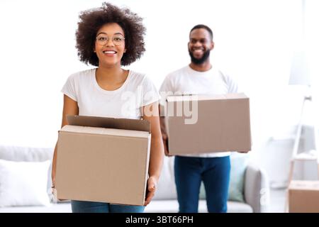 Black Couple Moving Carrying Packed Cardboard Boxes Into New Home Stock Photo