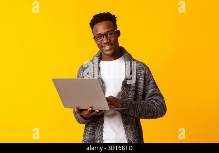 Handsome young african man using laptop on yellow Stock Photo