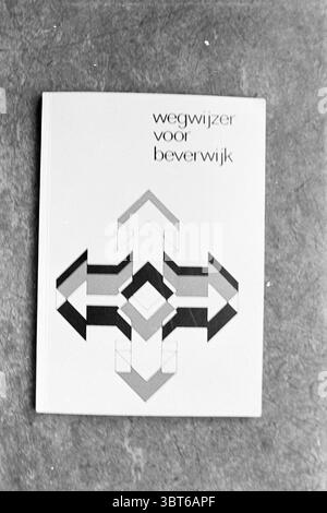 Signpost for Beverwijk, Whizgle News, Dutch Desk, The Netherlands, 1950 - 2000 in 1972. These topics are shown in the image. The scene features a simple, rectangular object resting on a textured surface. The object is predominantly white with a geometric design that includes an array of arrows and shapes, displayed in shades of gray and black. The arrows point in various directions, suggesting movement and choice. The composition of the object is centered and symmetrical, creating a sense of balance. The background is a muted, darker shade, contrasting with the lighter design of the object. Th Stock Photo