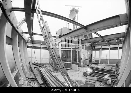 Demolition renovation of lock tower, Whizgle News, Dutch Desk, The Netherlands, 1950 - 2000 on 29-01-1992. These are the elements in the image. The scene depicts an industrial interior that is in the midst of construction or renovation. The space features exposed metal beams and structural elements, showcasing a raw, unfinished aesthetic. A large section of the roof is missing, allowing for an expansive view upward, where a large satellite dish or communication device is mounted high above, casting a shadow on the surrounding surfaces. Scattered throughout the area are various construction mat Stock Photo