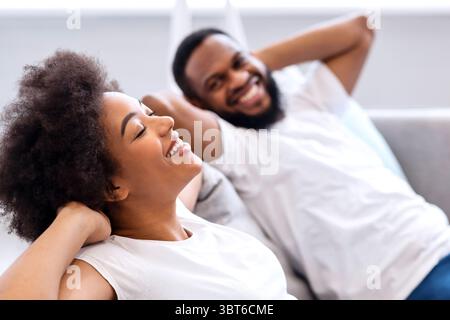 Happy Black Couple Resting Sitting On Sofa At Home Stock Photo