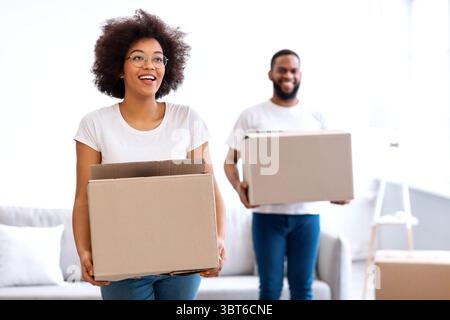 Joyful Black Spouses Carrying Moving Boxes Entering New Home Together Stock Photo