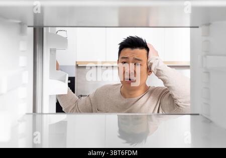Shocked chinese man looking inside empty fridge Stock Photo