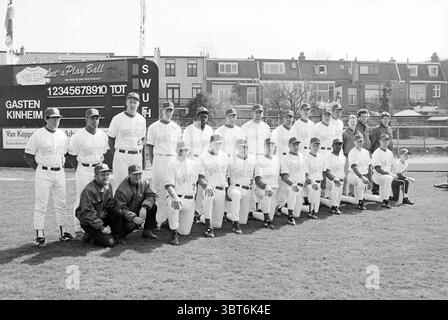 Baseball: team Kinheim, Whizgle News, Dutch Desk, The Netherlands, 1950 - 2000 on 13-04-1996. These are the topics in the image. In a lively outdoor setting, a team of baseball players is assembled, showcasing a mix of uniforms with clean white shirts adorned with colorful graphics. The players are positioned in a tight formation, arranged in two rows, with the back row standing and the front row crouched slightly, all displaying focused expressions. The backdrop features a classic baseball field, with well-maintained green grass underfoot. Behind the players, a large scoreboard stands out, re Stock Photo