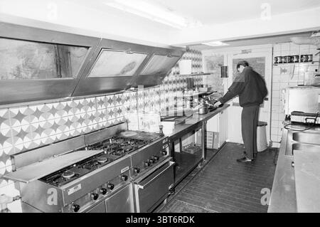 Foreclosure sale Coninckshoek Sale Haarlem Koningstraat The Netherlands, Whizgle News, Dutch Desk, The Netherlands, 1950 - 2000 on 18-03-1988. These topics appear in the image. The scene presents a black-and-white kitchen, characterized by a mix of industrial and homey elements. The kitchen is spacious but appears somewhat cluttered, illuminated by overhead fluorescent lights that cast a stark glow across the space. To the left, a long metal countertop, lined with a series of cooking appliances, features a large gas stove with multiple burners, their knobs glinting softly in the light. The sur Stock Photo