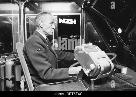 Driver behind the wheel Noord Zuid Hollandse Vervoersmaatschappij N.V. NZ, Whizgle News, Dutch Desk, The Netherlands, 1950 - 2000 on 15-10-1970. These topics appear in the image. The scene features a mature man seated at the controls of a vehicle, exuding an air of concentration and professionalism. He has a stern yet focused expression, suggesting a deep sense of responsibility for his task. His attire is formal, suggesting he holds a position of authority or experience in his role. The interior of the vehicle is structured and utilitarian, showcasing an array of instruments and control panel Stock Photo