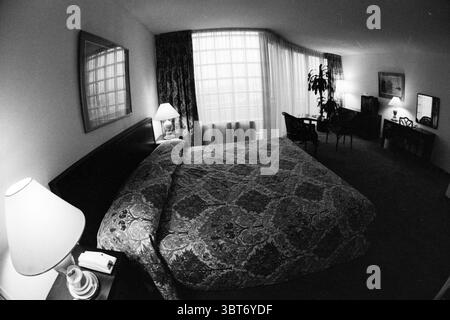 Room hotels Hotel page, Whizgle News, Dutch Desk, The Netherlands, 1950 - 2000 on 19-12-1990. These are the topics in the image. The scene presents a cozy bedroom with a warm and inviting atmosphere. The focal point is a large bed dressed in a richly patterned quilt featuring intricate designs in various shades of beige and brown. The bed is framed by a dark wooden headboard, adding a touch of elegance to the overall aesthetic. To the left, a soft light emanates from a bedside lamp, its warm glow contrasting with the cooler light filtering in from a large window on the far wall. The window is Stock Photo
