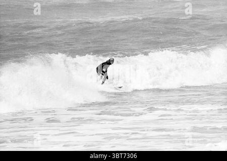 Surfer at sea, Whizgle News, Dutch Desk, The Netherlands, 1950 - 2000 on 03-04-1995. These topics are shown in the image. The scene captures a dynamic moment at the beach, where the powerful ocean waves create a dramatic backdrop. In the foreground, a lone surfer is skillfully balancing on a surfboard, leaning slightly forward as they ride the crest of a wave. The surfer is clad in a dark wetsuit, which contrasts sharply against the frothy, white surf. The waves are thick and rolling, their foamy tops glistening under a muted sky, suggesting an overcast or possibly hazy day. The water is a mix Stock Photo