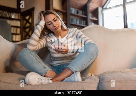 Worried confused lady using cellphone, looking at screen Stock Photo