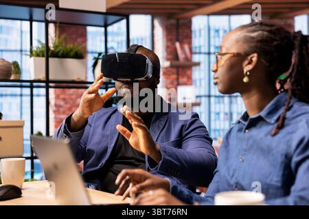 Black people integrates VR and AI into their daily routine where the man engages in immersive 3D experience. Young focused woman managing the animation within the metaverse on laptop. Stock Photo