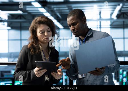 System administrators in data center using devices, executing security patches, verifying firewall configurations. Teamworking IT experts performing equipment vulnerability scans in server hub Stock Photo
