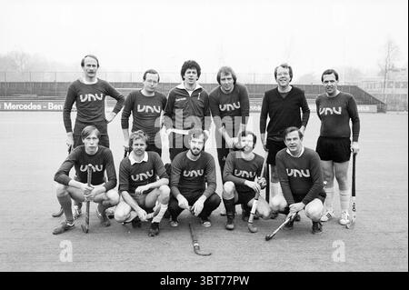 Hockey team VNU Hockey VNU Association of Dutch Publishers, Whizgle News, Dutch Desk, The Netherlands, 1950 - 2000 on 27-02-1982. The image includes these topics. In a sports setting, a group of ten individuals poses in two rows. The background features a blurred sports field, giving a sense of an outdoor area likely used for field hockey or a similar sport, characterized by a smooth surface and distant goal posts. The team members wear matching dark shirts featuring the letters 'UNU' prominently displayed on the front. The shirts have a classic cut, with short sleeves and a simple design, lik Stock Photo