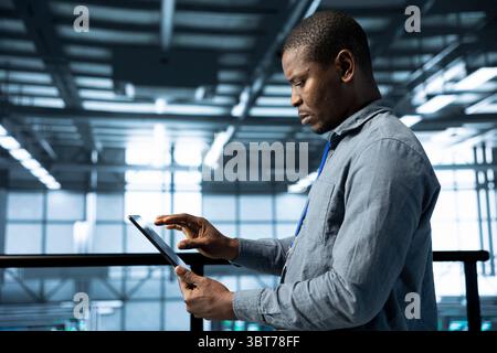 Engineer in data center with tablet integrating AI driven automation tools, running predictive maintenance routines. Man ensuring continuous uptime of server room, managing data flows Stock Photo