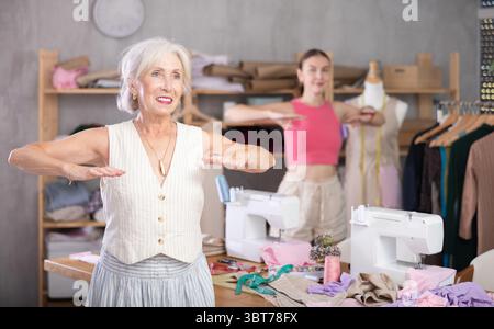 Elderly and adult women doing warm-up exercises in sewing workshop Stock Photo