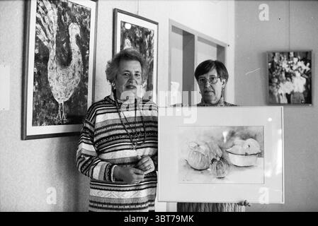 Sisters v.d. Heart exhibition Heemstede Heemstede The Netherlands, Whizgle News, Dutch Desk, The Netherlands, 1950 - 2000 on 04-05-1997. These topics are shown in the image. In the scene, two women stand side by side, showcasing a framed piece of art that features a watercolor depiction of several onions and a pear. The first woman on the left has a cheerful expression, adorned in a striped sweater with a mix of muted colors, including blue, white, and earthy tones. She has short, light-colored hair and wears long earrings that catch the light subtly. The woman on the right, also smiling, is d Stock Photo