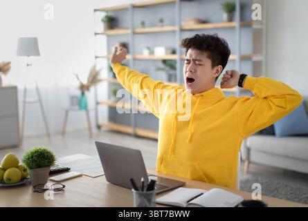 Asian male student yawning sitting at desk with pc Stock Photo
