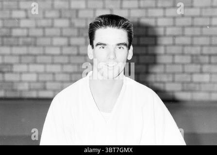 12 difference. judoka's kenamju portraits + group Judo, Whizgle News, Dutch Desk, The Netherlands, 1950 - 2000 on 03-11-1989. These are the topics in the image. The scene features a young man with short, neatly styled dark hair and a confident expression. He is wearing a white martial arts uniform, characterized by a simple yet distinct design that conveys a sense of discipline and focus. The fabric appears crisp and well-maintained, reflecting the seriousness of his training. The background consists of a brick wall with a repetitive pattern of dark and light bricks, adding a textured and stru Stock Photo