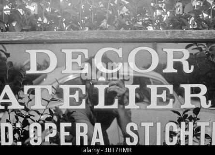 Sign stage decor Signs, Whizgle News, Dutch Desk, The Netherlands, 1950 - 2000 on 13-08-1973. The image contains these topics. The scene captures a reflection in a polished surface, showcasing a grassy area and elements of nature surrounding it. The foreground features large, bold letters that spell out a word, prominently displayed across the center. These letters are painted in a stark contrast against a darker background, giving them a bold, eye-catching appearance. In the background, the greenery is lush, with various shades of green creating a vibrant contrast to the lettering. The foliag Stock Photo