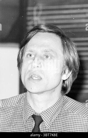 Portrait of the director of Fesam Haarlem The Netherlands ., Whizgle News, Dutch Desk, The Netherlands, 1950 - 2000. These are the topics in the image. The scene features a man with light-colored hair, styled in a way that appears slightly tousled. He is dressed in a checkered shirt with a visible pattern consisting of thin lines in contrasting colors, complemented by a solid tie. His expression suggests he is engaged in a thoughtful discussion, with his mouth slightly open as if he is in the midst of speaking. The background is subtly blurred, likely featuring neutral tones that do not distra Stock Photo