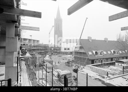 New construction project homes Beverwijk Beverwijk The Netherlands, Whizgle News, Dutch Desk, The Netherlands, 1950 - 2000 on 04-1984. These topics appear in the image. The scene captures a bustling construction site, dominated by a gray and overcast sky that imparts a moody atmosphere. In the foreground, the skeletal framework of a building is prominent, characterized by exposed concrete beams and vertical supports reaching upward. Scattered around the site are various construction materials: stacks of timber, metal scaffolding, and piles of bricks, all contributing to the sense of ongoing wo Stock Photo