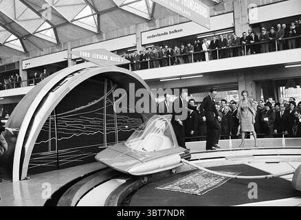 AutoRai. Opening by Prince Bernhard Amsterdam Europaplein 24 The Netherlands, Whizgle News, Dutch Desk, The Netherlands, 1950 - 2000 in 1961. These topics appear in the image. The scene captures a bustling exhibition setting featuring a futuristic display. Prominent in the foreground is a sleek, rounded vehicle gliding onto a circular platform, showcasing its innovative design. The vehicle has smooth lines and a metallic finish, accentuating the era's aspiration toward advanced technology. Surrounding this centerpiece are various architectural elements, including a curved structure that rises Stock Photo