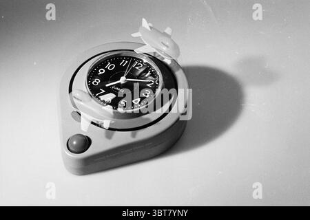 KLM alarm clock, Whizgle News, Dutch Desk, The Netherlands, 1950 - 2000 on 04-10-1994. These are the topics in the image. The scene features a unique alarm clock situated on a smooth, light-colored surface. The clock itself has a round shape with a black dial that stands out prominently against the softer hues of its casing. The face of the clock is adorned with white numerals and slender clock hands, which harmonize with the black background, creating a striking contrast that draws the eye. Two small airplane figures are playfully positioned on top of the clock, contributing a whimsical eleme Stock Photo