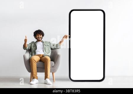 Handome young indian man pointing at huge smartphone, mockup Stock Photo