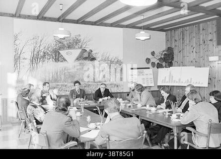 Vicon agricultural machine factory Nieuw-Vennep press conference? Nieuw-Vennep, Whizgle News, Dutch Desk, The Netherlands, 1950 - 2000 on 02-1977. These are the topics in the image. In this setting, a large conference room is filled with a long rectangular table surrounded by numerous people engaged in discussion. The room features a warm wooden paneling on the walls, creating a cozy and inviting atmosphere. Above, a series of overhead lights provide soft illumination, enhancing the sense of focus on the meeting. At the center of the table are neatly arranged cups and saucers, hinting at the p Stock Photo