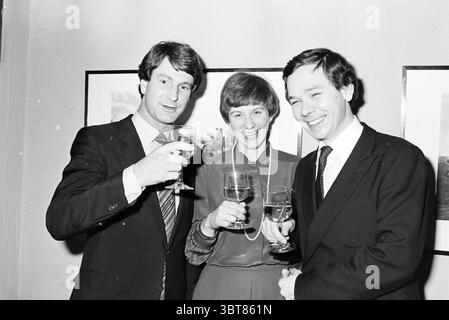 Alliance lunch Laren NH Restaurant Laren, Whizgle News, Dutch Desk, The Netherlands, 1950 - 2000 on 14-01-1980. These topics appear in the image. The scene captures three individuals standing closely together, exuding a sense of camaraderie and celebration. The two men on either side are neatly dressed in tailored suits, emphasizing a formal yet approachable atmosphere. One man has dark hair and a hint of a smile, while the other has lighter hair and presents a wide, cheerful grin. The woman in between them is wearing a stylish outfit with a high neckline, accentuated by a strand of pearls aro Stock Photo