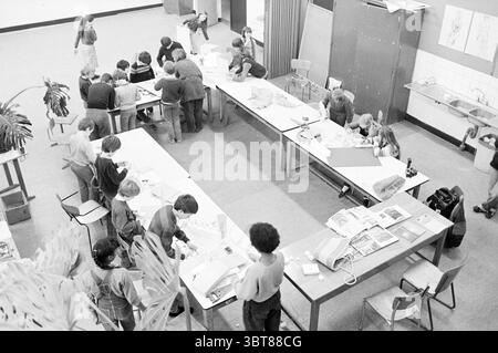 Montessori school near Kreater Schools, Whizgle News, Dutch Desk, The Netherlands, 1950 - 2000 on 30-01-1981. These topics are shown in the image. In a spacious classroom filled with an air of creativity and collaboration, small groups of children are engaged in various activities. The layout of the room is open, featuring a central area with several long, rectangular tables arranged in a way that invites teamwork. The tables are cluttered with an assortment of craft materials—colored paper, scissors, glue, and various tools. Some children are intently working on projects, while others seem to Stock Photo