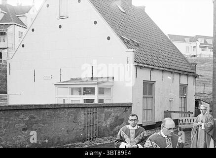 Initiation of pastor Wijk aan Zee Clergy Initiation, Whizgle News, Dutch Desk, The Netherlands, 1950 - 2000 on 06-04-1968. These are the elements in the image. In a quaint setting, a small, white, gabled house stands prominently, its simplicity accentuated by its weathered exterior and distinct roofing tiles. The structure showcases a mix of traditional and modern architectural elements, highlighted by a series of round black dots seemingly punctuating the smooth surface of the wall. In the foreground, two individuals move together, dressed in ceremonial robes adorned with rich, ornate pattern Stock Photo