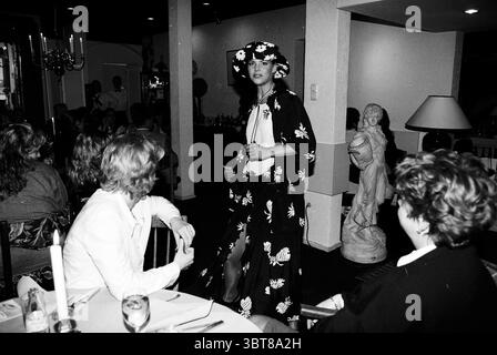 Fashion show Queenie Zandvoort Zandvoort, Whizgle News, Dutch Desk, The Netherlands, 1950 - 2000 on 16-04-1997. These topics appear in the image. The scene captures an indoor social gathering with a blend of elegance and casual celebration. Dominating the foreground is a model, dressed in a striking, floral-patterned outfit that contrasts with the surrounding decor. The outfit features a flowing silhouette, enhancing the sense of movement as she poses confidently. Surrounding her are several onlookers seated at a table adorned with white tablecloths. Their attire varies from smart casual to sl Stock Photo