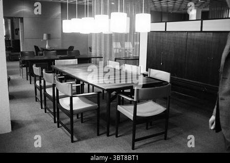 Danish furniture show Furniture furniture, Whizgle News, Dutch Desk, The Netherlands, 1950 - 2000 on 02-04-1964. These are the topics in the image. The scene showcases a spacious, well-lit interior that exudes a modern, minimalist aesthetic. The focal point is a long, rectangular table made of dark wood, surrounded by sleek, contemporary chairs with wooden frames and light, cushioned seats. The arrangement of the chairs suggests a setting meant for gatherings or conversations, with a total of eight positioned around the table. Above the table, a series of pendant lights hang down, their white, Stock Photo