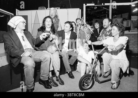 Theater group 'Momus' IJm. IJmuiden The Netherlands, Whizgle News, Dutch Desk, The Netherlands, 1950 - 2000 on 24-05-1995. These topics appear in the image. The scene is lively and filled with a sense of camaraderie among a diverse group of individuals. In the foreground, a man is seated with a playful expression, wearing a unique hat. He holds a gaming controller, clearly engaged in some lighthearted banter. To his right, a woman with dark, flowing hair is animatedly speaking, her gestures punctuating the excitement of the moment. Surrounding them are several others, each displaying a distinc Stock Photo