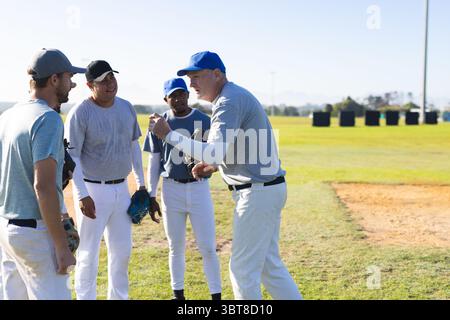 Diverse male baseball team standing and gesturing on baseball field with gloves near infield Stock Photo