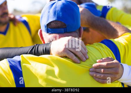 Senior male teammates huddling before game on baseball field wearing yellow jerseys and blue cap Stock Photo