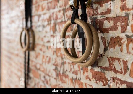 Wooden gymnastic rings hanging from black straps on exposed brick wall inside fitness studio Stock Photo