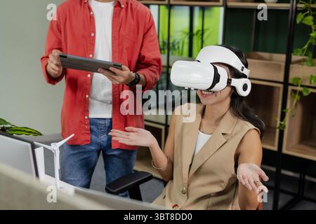 Asian coworkers wearing VR headset and using tablet at office desk with wind turbine model Stock Photo