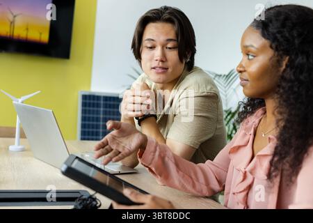 Diverse male colleagues examining wind turbine model at modern office using digital tablet Stock Photo